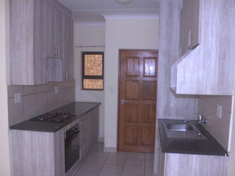 A functional galley-style kitchen featuring light wood-look cabinetry, dark countertops, a built-in oven with gas hob, and tiled flooring.