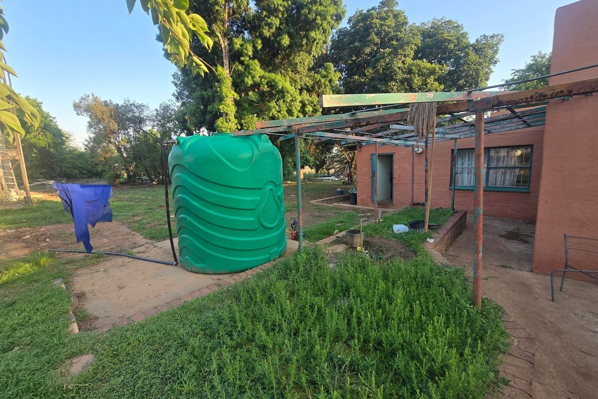 Rear exterior view of the farm property featuring a large water storage tank and a weathered metal pergola structure.