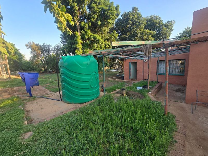 Rear exterior view of the farm property featuring a large water storage tank and a weathered metal pergola structure.