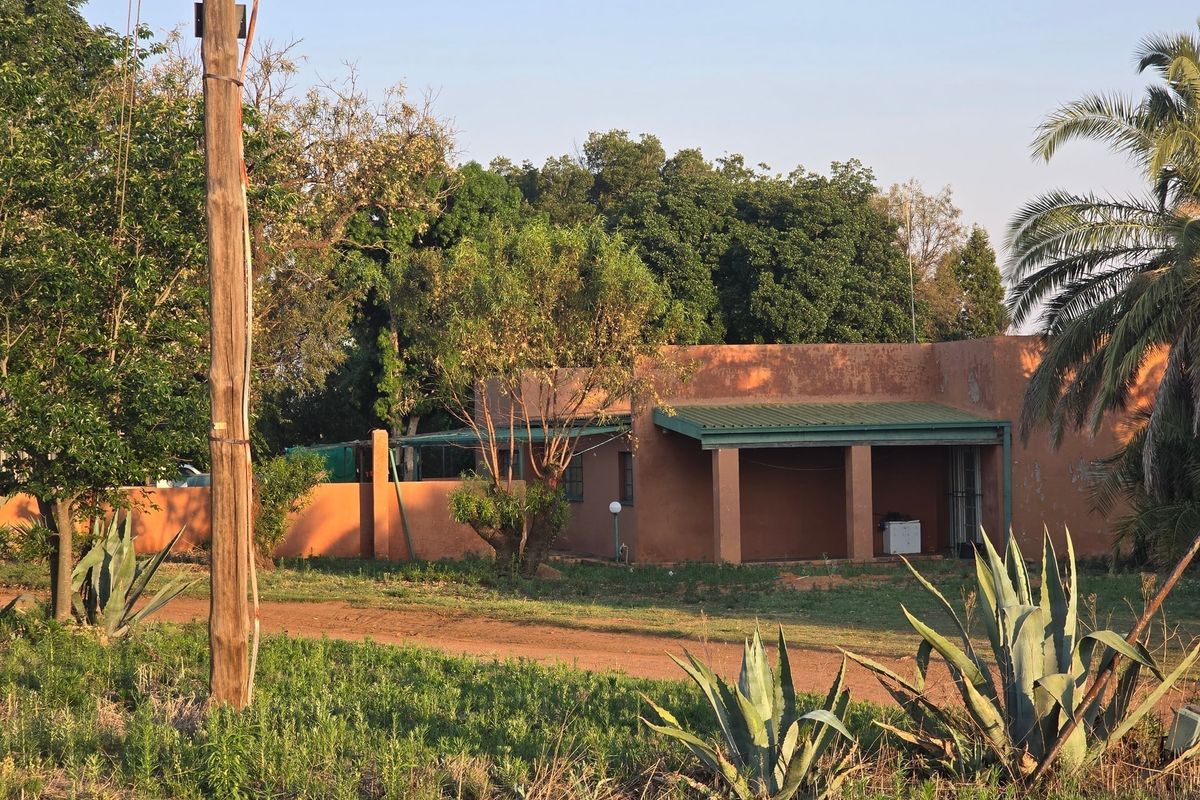 A view of the rear exterior of the farm building, featuring a covered patio area, perimeter wall, and mature garden surroundings.