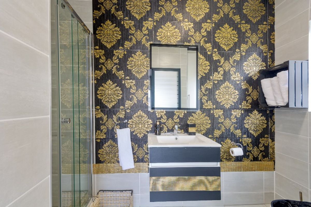 A bathroom featuring a glass shower enclosure, a modern wall-mounted vanity with basin, and bold decorative patterned wall tiles.