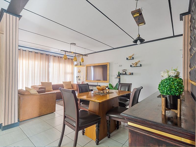 An open-plan living and dining area featuring tiled flooring, decorative ceiling detailing, and modern pendant lighting, creating a cohesive and functional space.