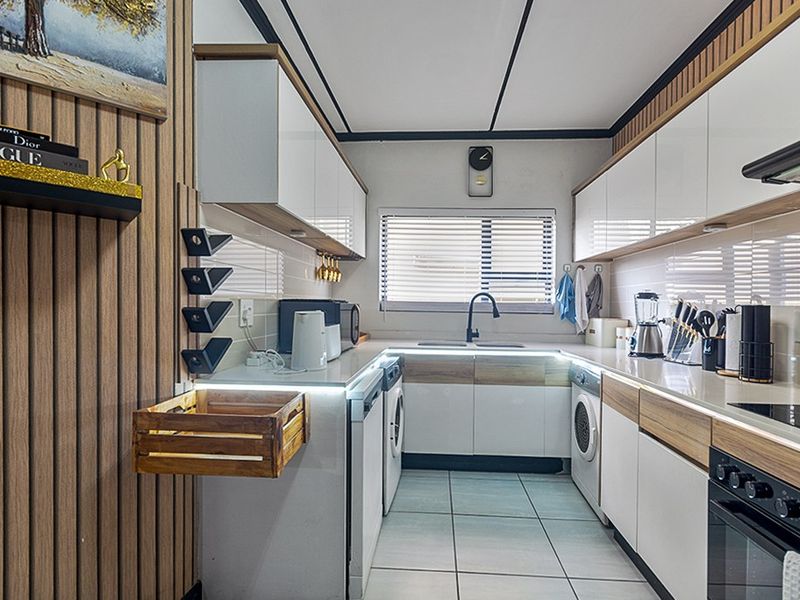 Modern galley-style kitchen featuring sleek white and wood-tone cabinetry, integrated appliances, under-cabinet lighting, and tiled flooring with a clean, contemporary finish.