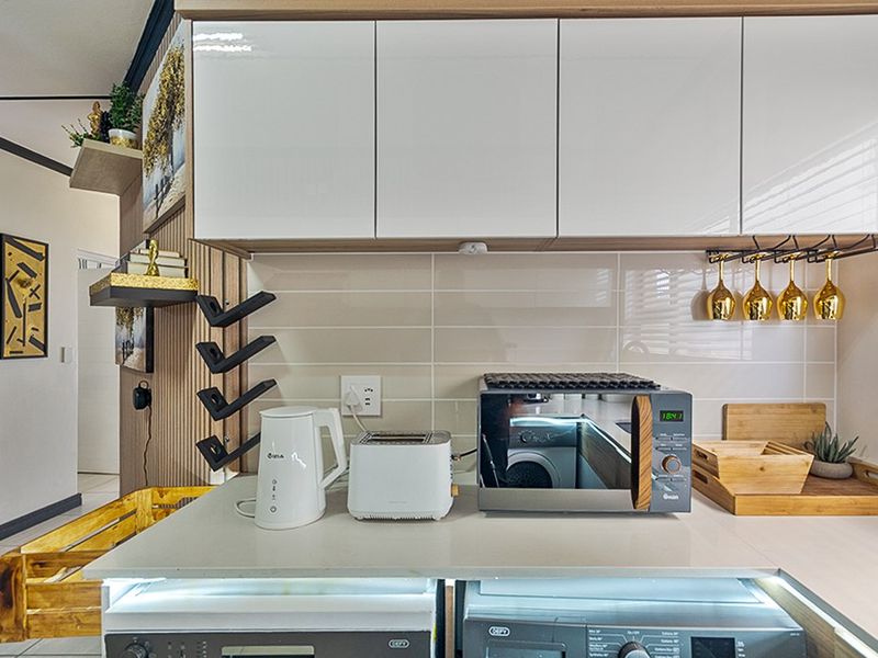 Modern kitchen area featuring glossy white cabinetry, stone countertops, subway tile backsplash, and integrated laundry appliances.