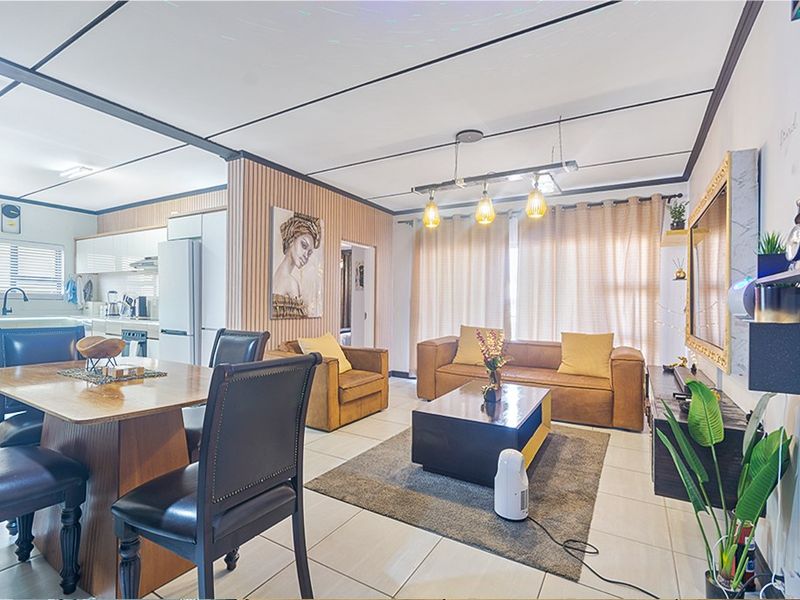 An open-plan living and dining area featuring tiled floors, slatted wall accents, and an integrated kitchen with modern cabinetry and built-in appliances.