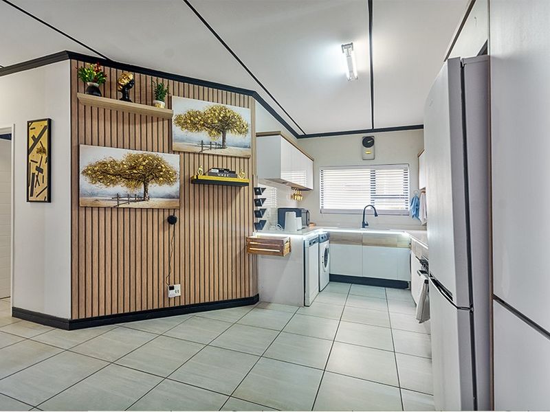 A modern kitchen featuring white cabinetry, tiled flooring, and a decorative slatted wood feature wall, creating a clean and contemporary cooking space.
