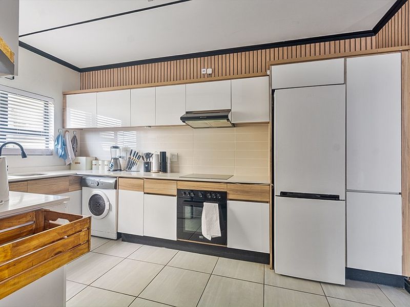 Modern kitchen featuring sleek white cabinetry, integrated appliances, wood-slat wall accents, and neutral tiled flooring, offering a clean and functional culinary space.