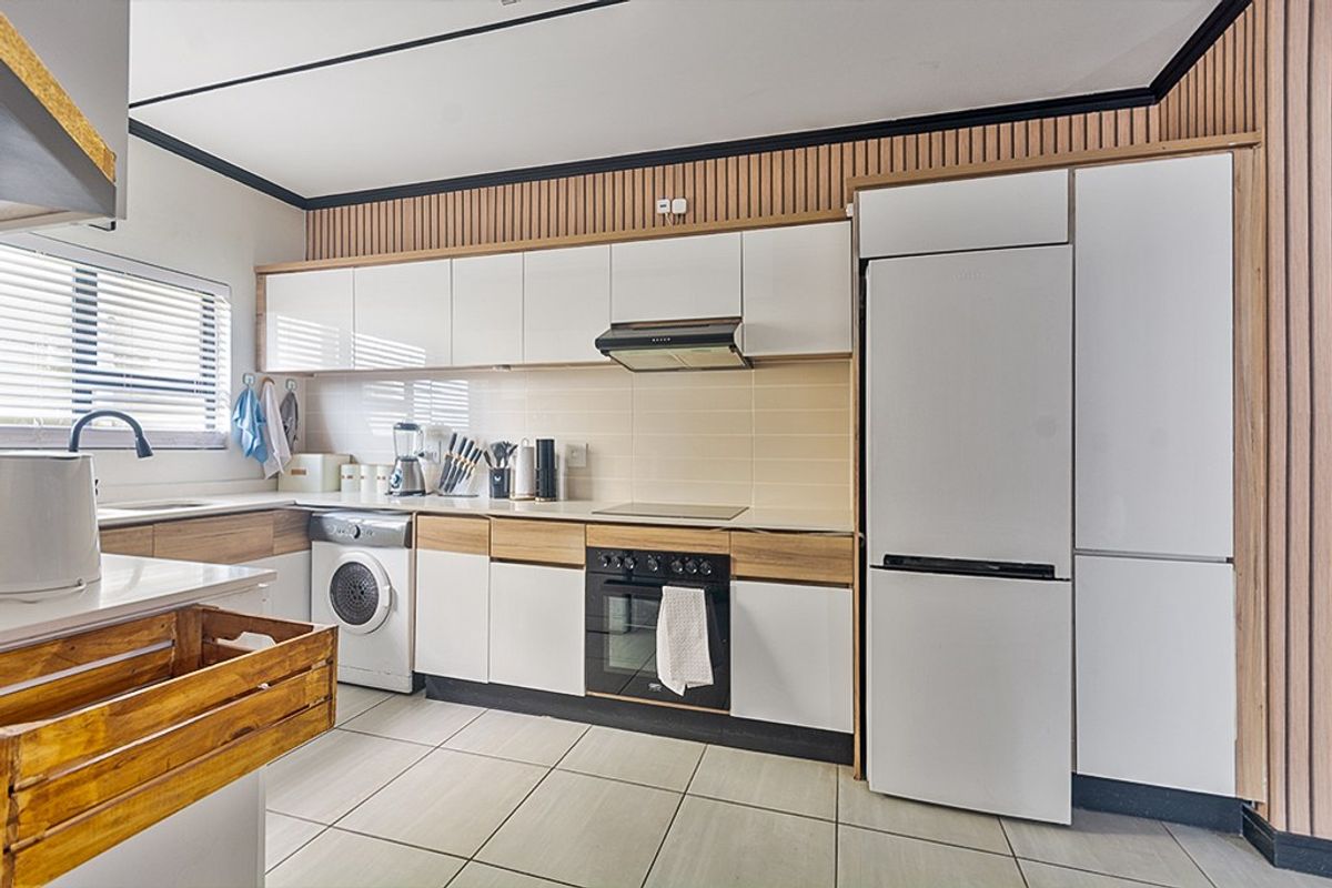 Modern kitchen featuring sleek white cabinetry, integrated appliances, wood-slat wall accents, and neutral tiled flooring, offering a clean and functional culinary space.