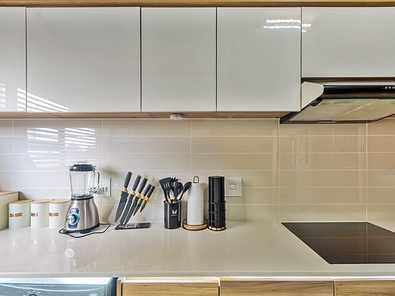 Modern kitchen featuring glossy white cabinetry, a sleek subway tile backsplash, stone countertops, and a built-in induction cooktop with an extractor fan.