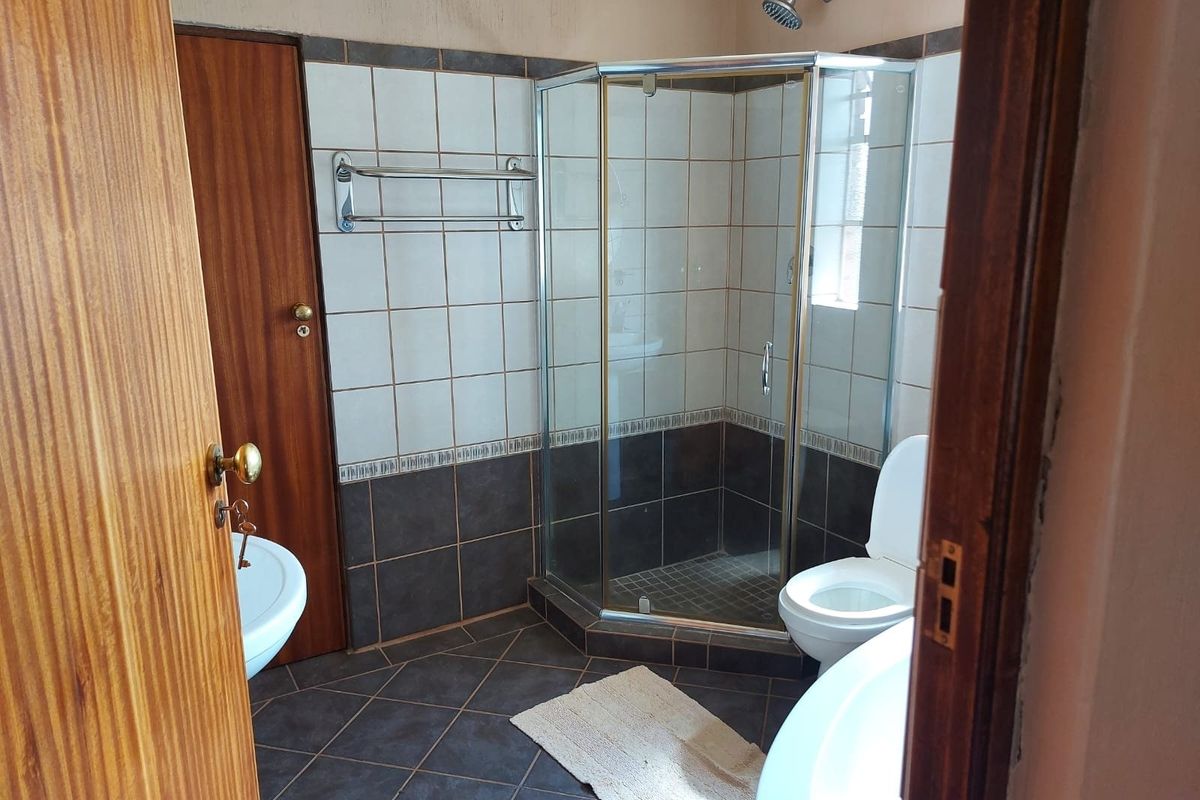 A functional bathroom featuring a corner shower enclosure, toilet, and tiled finishes, offering a practical layout with potential for cosmetic updates.