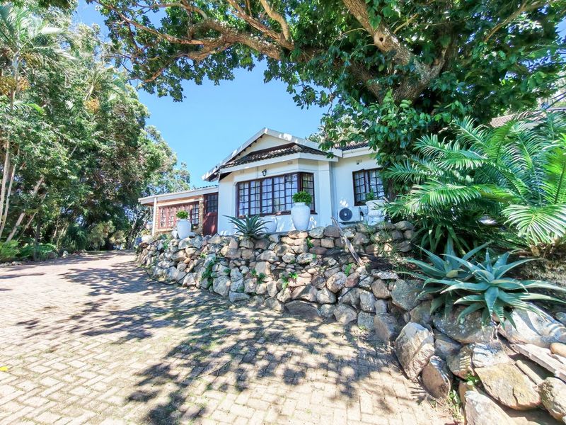 A charming single-story house featuring a stone retaining wall, paved driveway, and mature trees, showcasing a classic exterior facade.