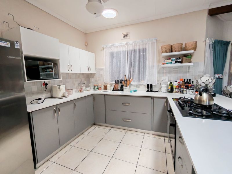 A functional kitchen featuring modern grey and white cabinetry, tiled flooring, a built-in gas hob, and ample counter space.