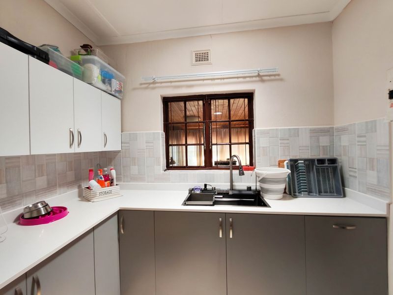 A functional laundry or scullery area featuring modern grey and white cabinetry, a dark composite sink, and tiled splashbacks.