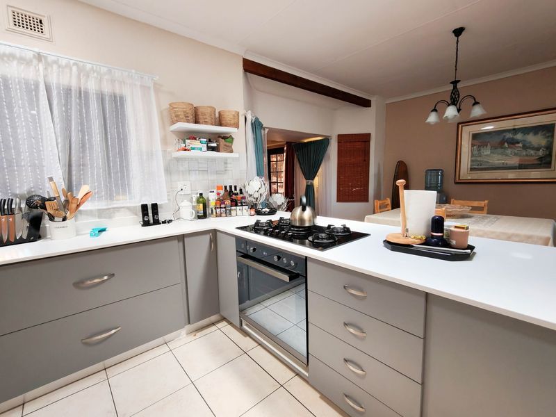 Modern kitchen featuring grey cabinetry, white countertops, a built-in gas hob, and an integrated oven, seamlessly flowing into the adjacent dining area.