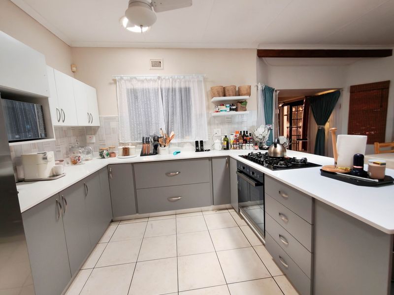 A functional kitchen featuring modern grey and white cabinetry, a built-in gas hob, oven, and tiled flooring with a breakfast counter.