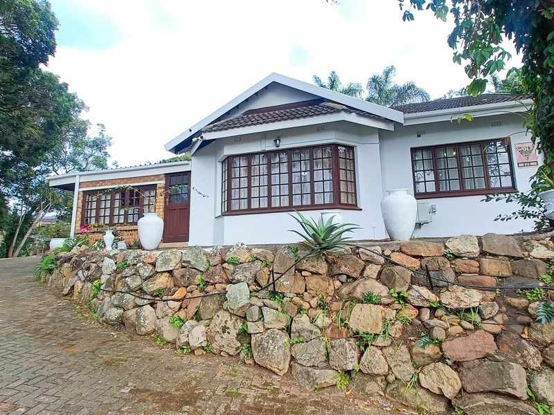 A charming single-story residence featuring a stone retaining wall, paved driveway, and classic timber-framed windows set within a lush, established garden.
