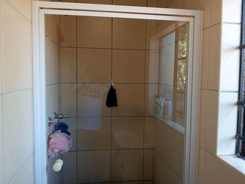 A functional shower enclosure featuring tiled walls and a window with security bars, providing a clean and practical space.