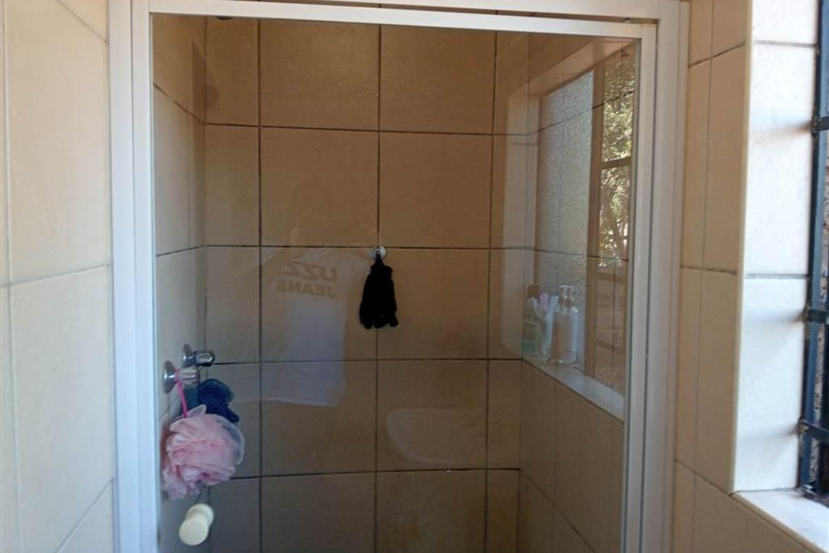 A functional shower enclosure featuring tiled walls and a window with security bars, providing a clean and practical space.