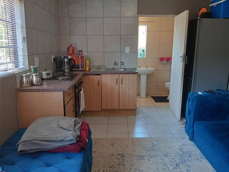 Open-plan living area featuring a compact kitchen with built-in cabinetry and hob, adjacent to a small bathroom with a pedestal basin and toilet.