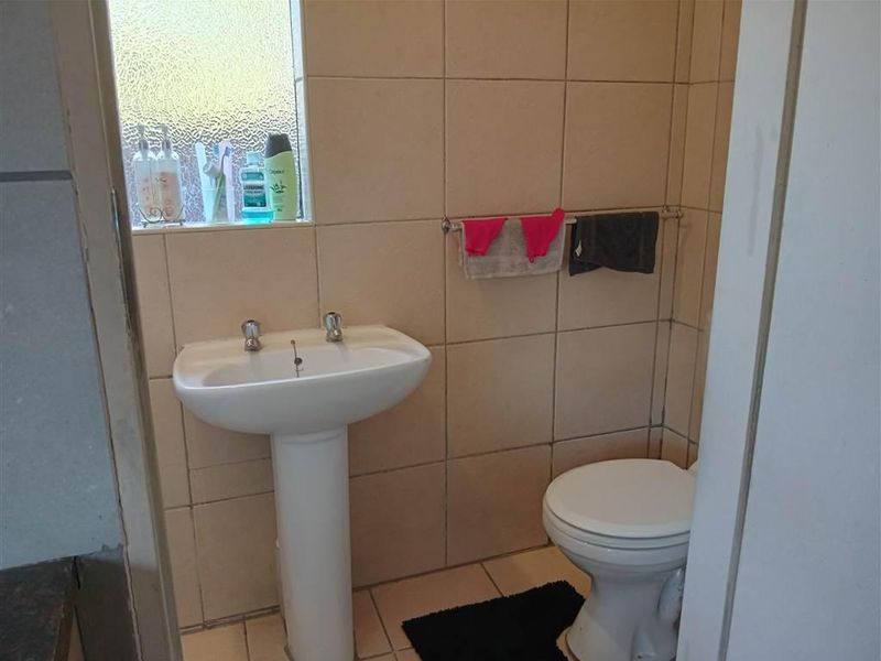 A functional bathroom featuring a pedestal basin, toilet, and neutral ceramic wall and floor tiling with an obscured glass window for privacy.