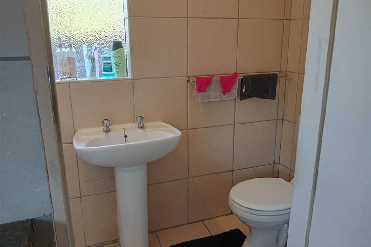 A functional bathroom featuring a pedestal basin, toilet, and neutral ceramic wall and floor tiling with an obscured glass window for privacy.