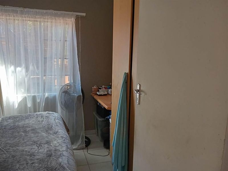 A bedroom featuring tiled flooring, a built-in wardrobe, and a window with sheer curtains.