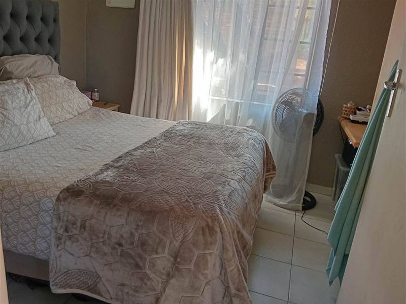 A standard bedroom featuring tiled flooring and large windows with curtain rails, providing natural light to the space.