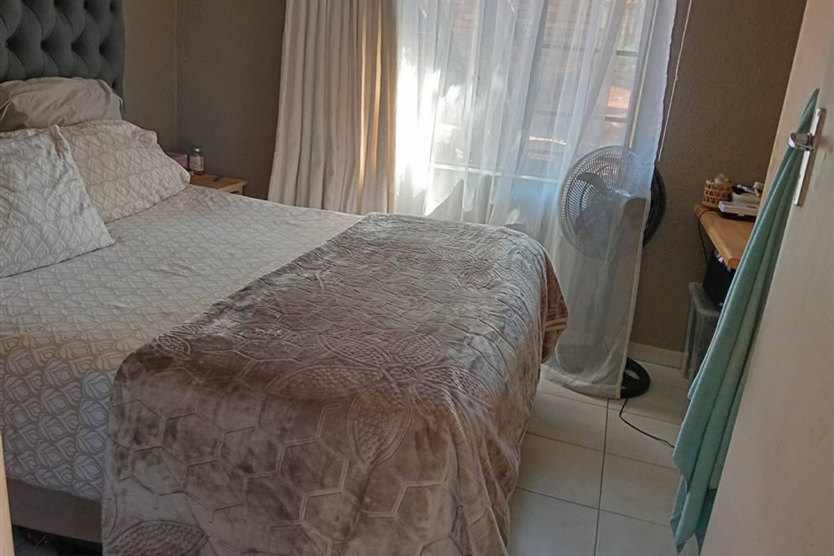 A standard bedroom featuring tiled flooring and large windows with curtain rails, providing natural light to the space.