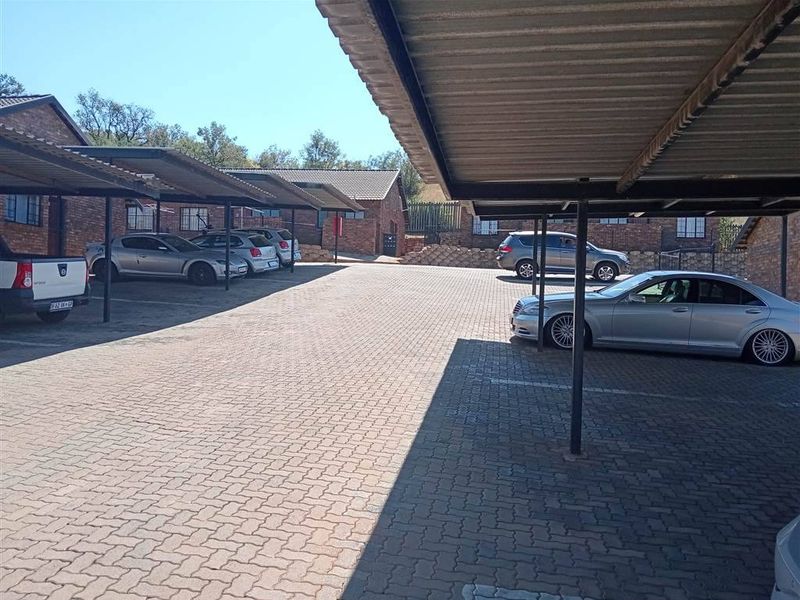 A paved outdoor parking area featuring multiple covered parking bays with metal roofing structures.