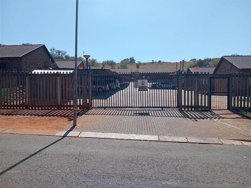 Front entrance view of a townhouse complex featuring a secure gated access point, paved driveway, and brick exterior walls.