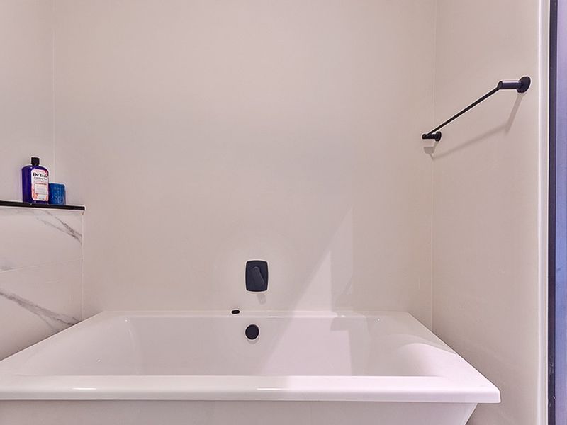 A clean, modern bathroom featuring a built-in bathtub with matte black fixtures and elegant marble-look tile detailing.