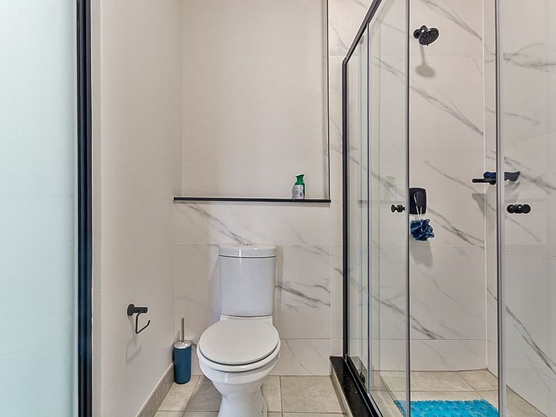 Modern bathroom featuring a glass-enclosed shower, marble-look wall tiling, and a standard toilet with built-in shelving.