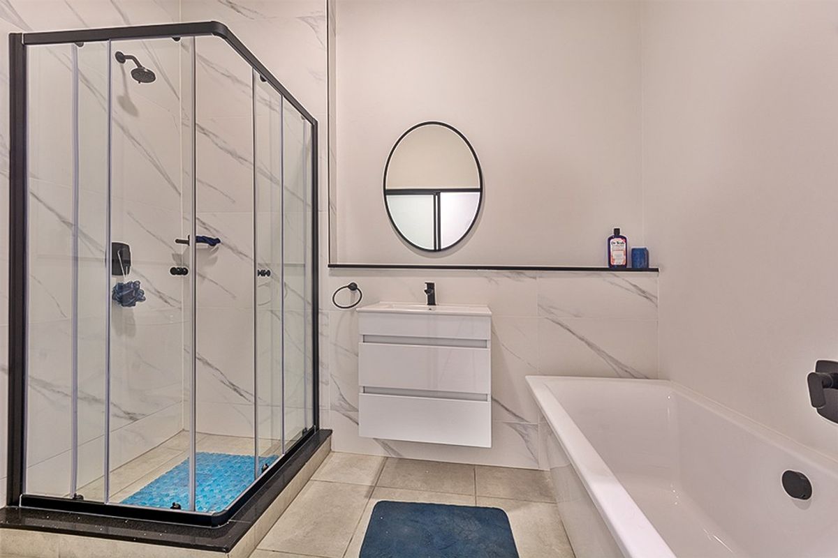 Modern bathroom featuring a glass shower enclosure, wall-mounted vanity with basin, and a bathtub, finished with elegant marble-look wall tiles and contemporary black tapware.