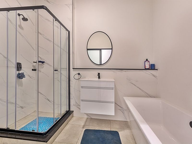 Modern bathroom featuring a glass shower enclosure, wall-mounted vanity with basin, and a bathtub, finished with elegant marble-look wall tiles and contemporary black tapware.