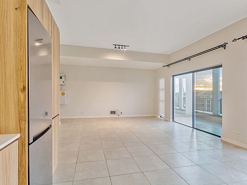 Spacious open-plan living area featuring neutral tiled flooring, modern built-in cabinetry, and large sliding glass doors leading to a private balcony.