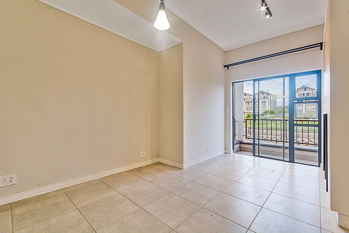 An empty, well-lit living area featuring neutral tiled flooring and a sliding glass door providing direct access to a private balcony.