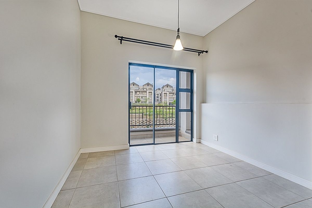 A bright, empty bedroom featuring neutral tiled flooring, a modern pendant light, and a sliding glass door providing access to a balcony.