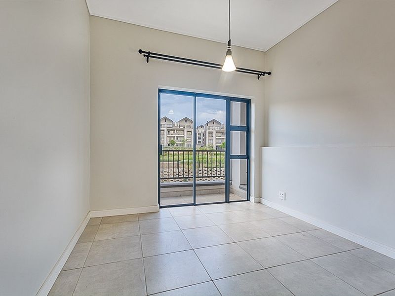 A bright, empty bedroom featuring neutral tiled flooring, a modern pendant light, and a sliding glass door providing access to a balcony.