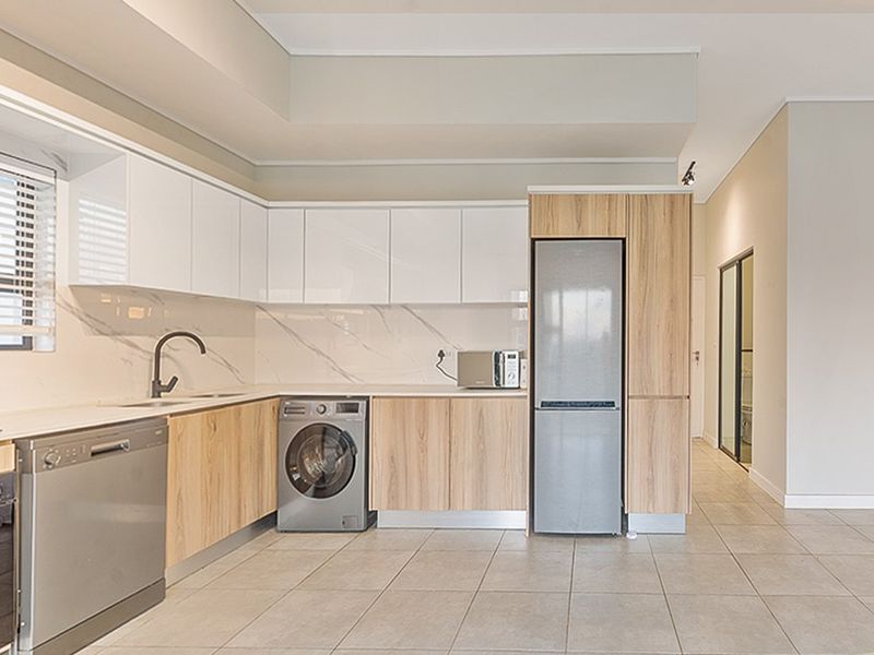 Modern kitchen featuring sleek white and wood-grain cabinetry, stone-look backsplash, integrated appliances, and neutral tiled flooring in an open-plan layout.