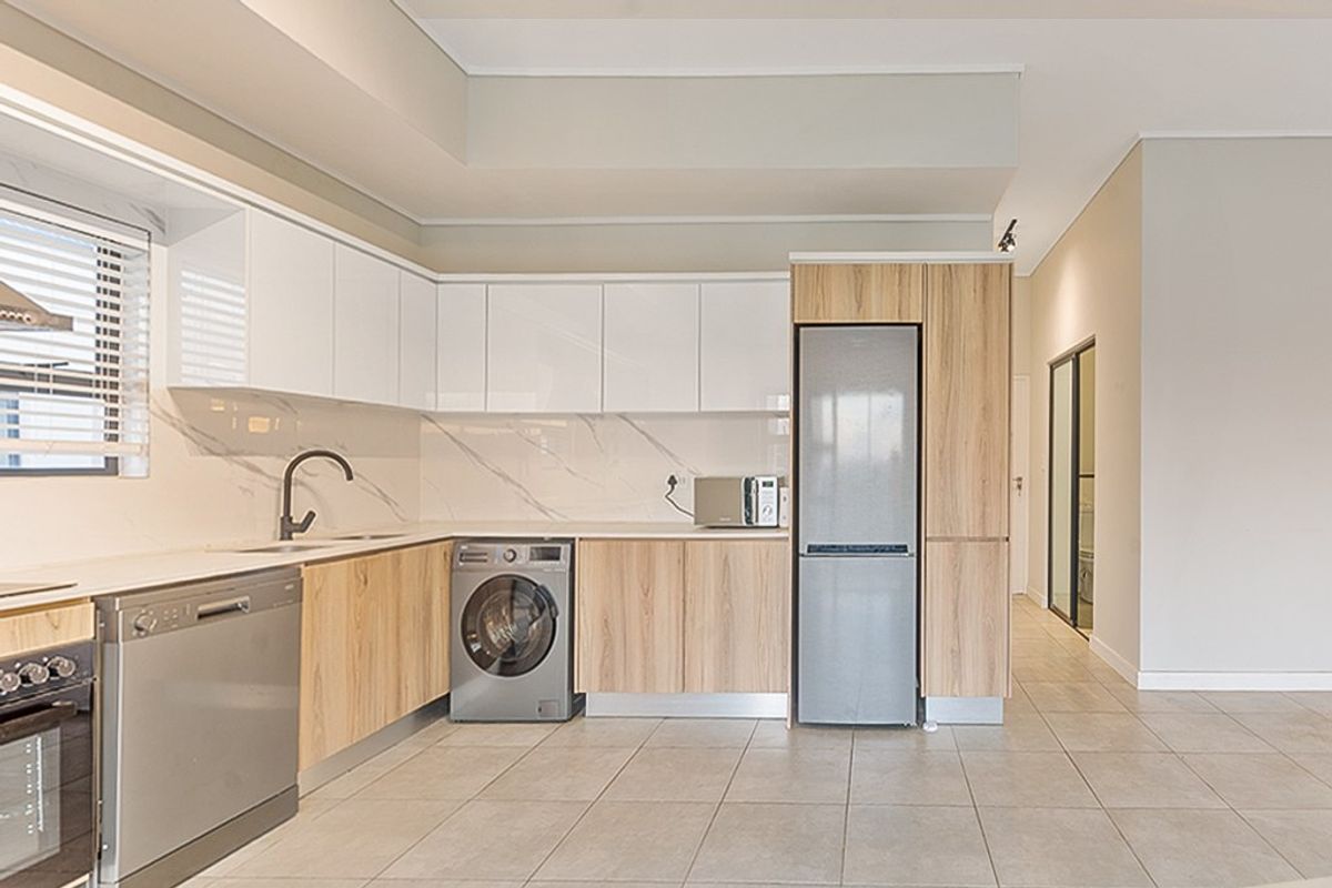 Modern kitchen featuring sleek white and wood-grain cabinetry, stone-look backsplash, integrated appliances, and neutral tiled flooring in an open-plan layout.