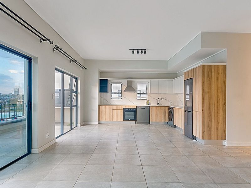 Modern open-plan kitchen and living area featuring sleek wood-finish cabinetry, integrated appliances, tiled flooring, and large sliding doors leading to a balcony.