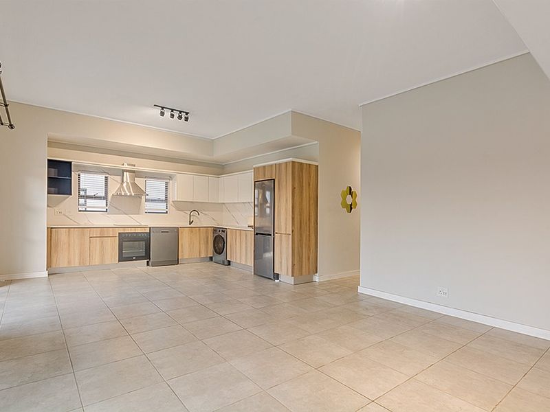 Spacious open-plan living area featuring a modern kitchen with built-in cabinetry, integrated appliances, and neutral tiled flooring throughout.