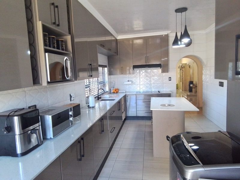 Modern kitchen featuring high-gloss cabinetry, stone countertops, a central island, and tiled finishes, leading through an archway to adjacent living spaces.