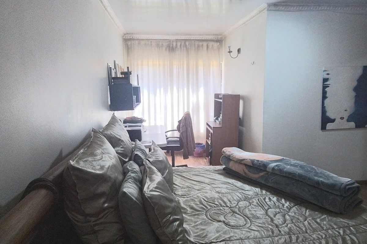 A bedroom featuring crown molding and a wall sconce, with a window covered by sheer curtains.