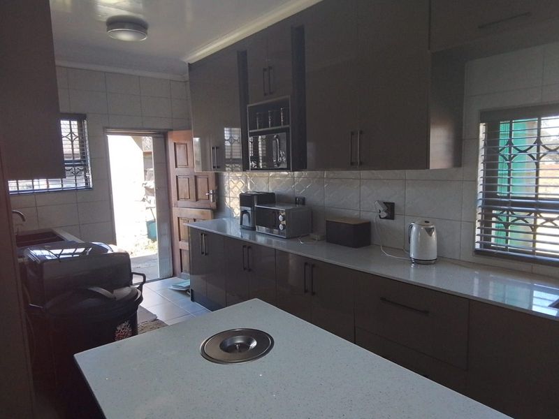 Modern kitchen featuring high-gloss cabinetry, stone countertops, a central island, and tiled backsplash with direct access to the exterior.