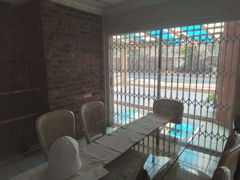 Dining area featuring an exposed brick wall and large sliding glass doors with security gates, providing direct access to the outdoor pool area.