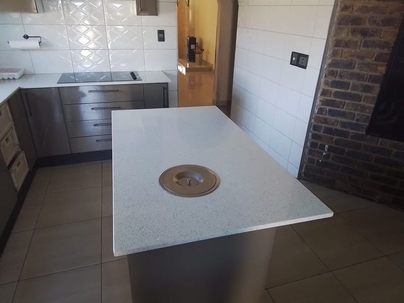Modern kitchen featuring a central island with a quartz countertop, built-in hob, tiled splashback, and an exposed brick feature wall.
