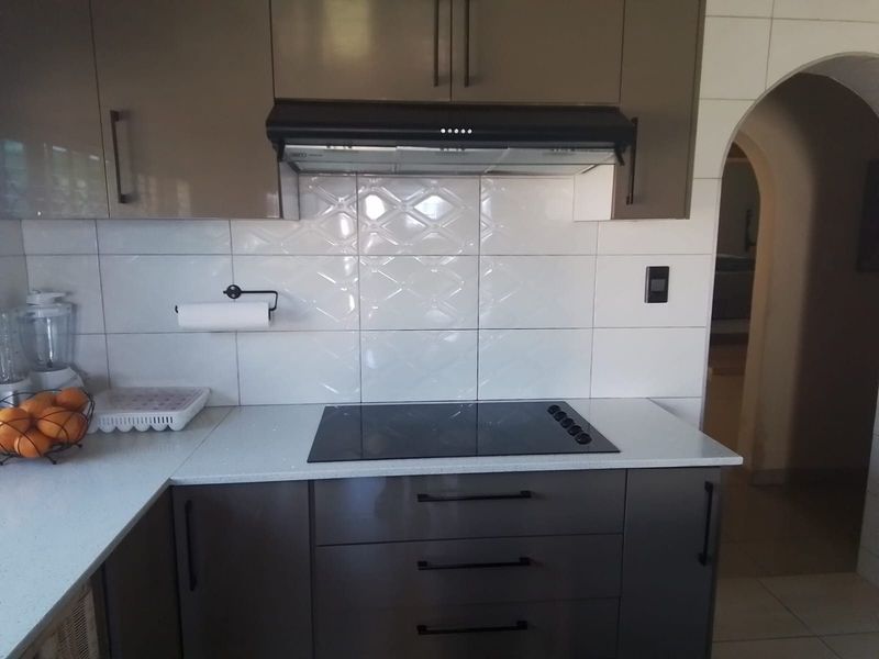Modern kitchen featuring sleek dark cabinetry, a white stone countertop, a built-in electric hob, and a matching extractor fan with a tiled backsplash.