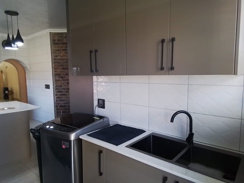 Modern kitchen featuring sleek grey cabinetry, a double basin sink with black fixtures, tiled splashback, and an exposed brick feature wall.