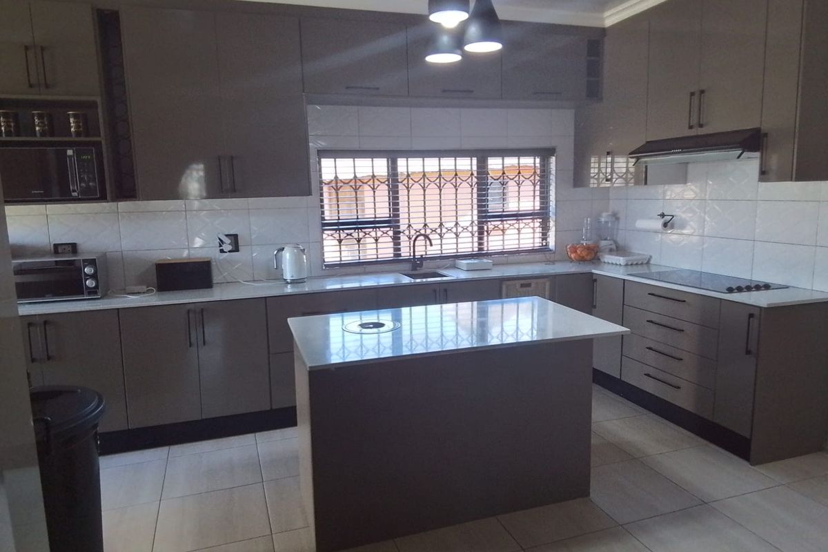 Modern kitchen featuring high-gloss cabinetry, a central island with stone countertops, tiled backsplash, and integrated cooking appliances.